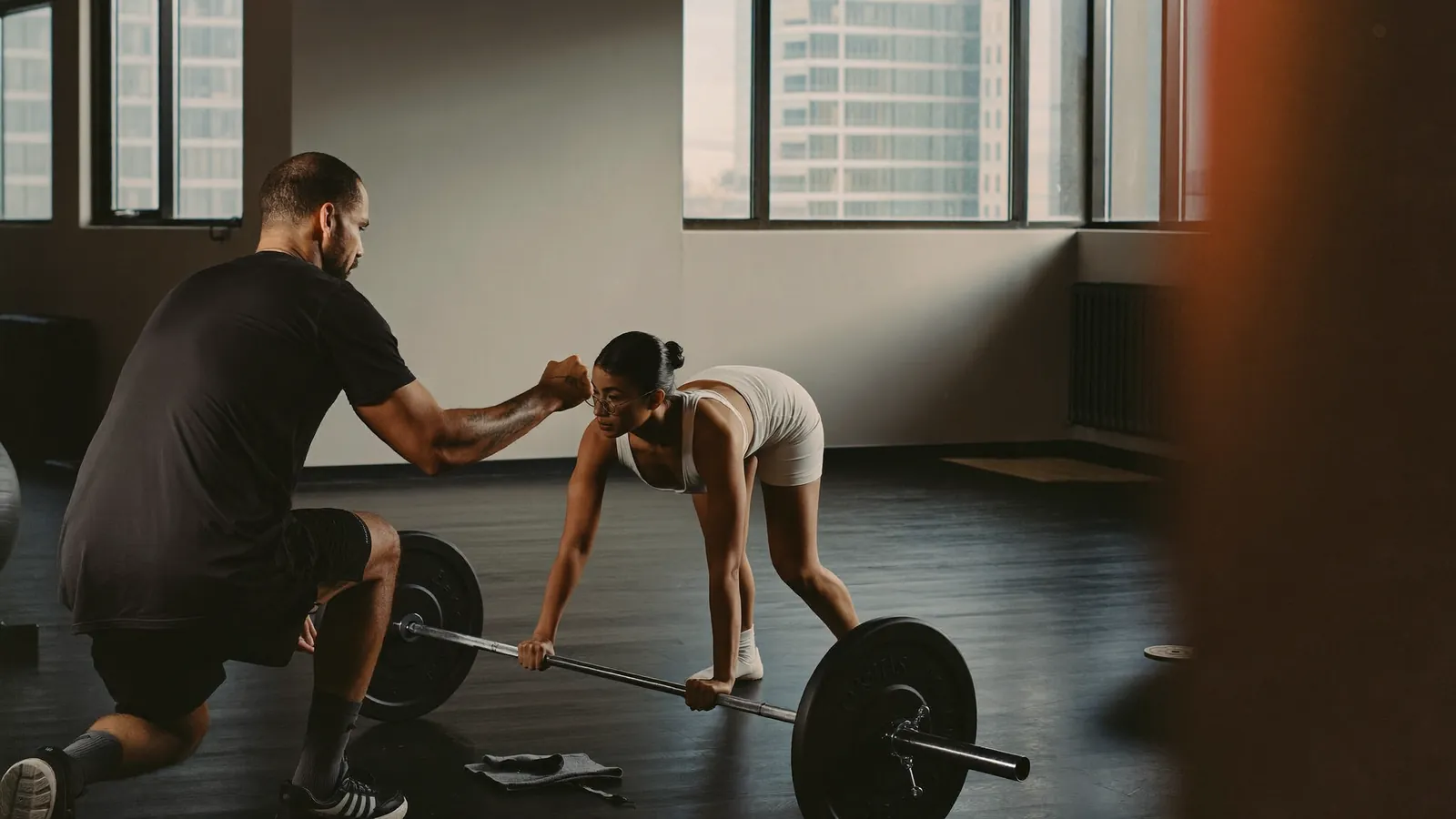 Personal trainer spotting a client on a barbell in a modern gym