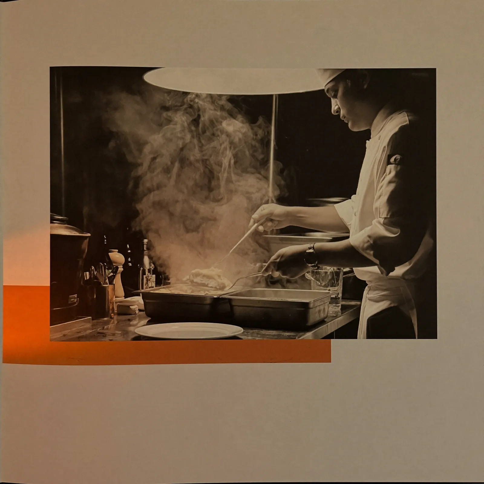Chef plating a dish in an open restaurant kitchen with steam rising